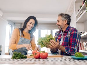 Mature man and woman making salad from fresh vegetables at home
